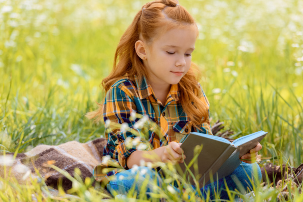 retrato de adorable pelo rojo libro de lectura infantil mientras está sentado en el campo de verano
 - Foto, Imagen