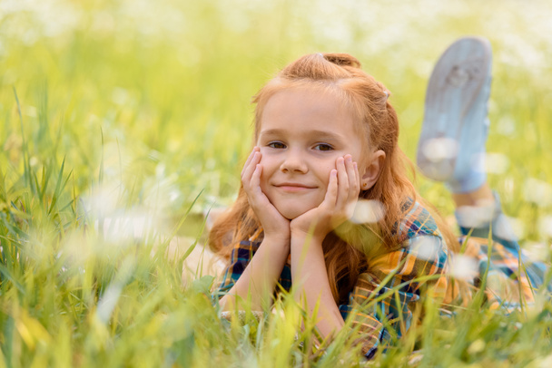 portrait of little smiling child resting on green grass in meadow - Photo, Image