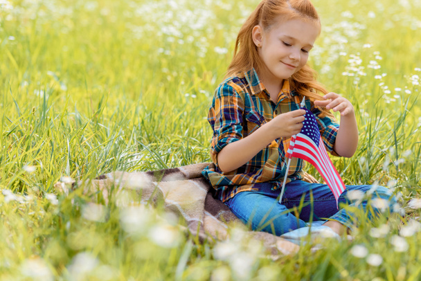 cute kid with american flagpole resting on green grass in field - Фото, зображення