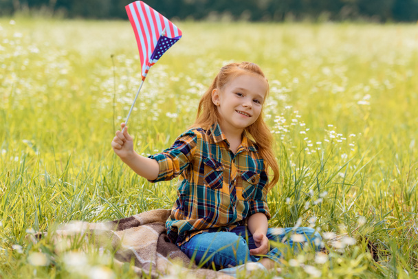 χαριτωμένο παιδί με αμερικανική κοντάρι σημαίας στηρίζεται σε πράσινο χόρτο πεδίο - Φωτογραφία, εικόνα