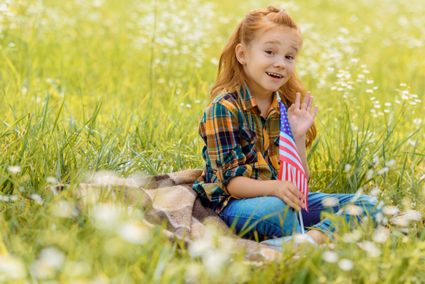emotional kid with american flagpole resting on green grass in field - Foto, afbeelding