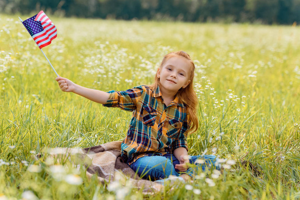 cute kid with american flagpole resting on green grass in field - Foto, Imagen