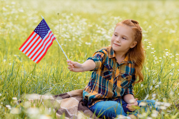lindo niño con el asta de la bandera americana descansando sobre hierba verde en el campo
 - Foto, imagen