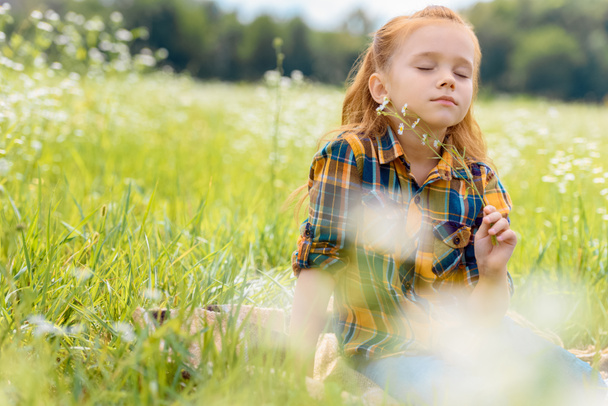 portrait of kid with eyes closed and wild flowers in hand resting in meadow - Foto, Imagem