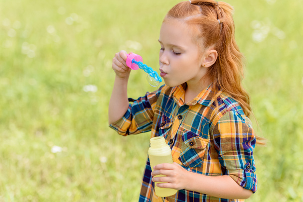 портрет ребенка, дующего мыльные пузыри на лугу
 - Фото, изображение