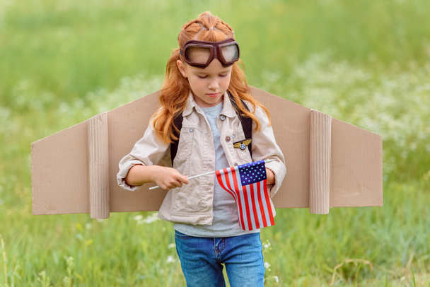 Porträt eines Kindes im Pilotenkostüm mit amerikanischem Fahnenmast auf einer Wiese - Foto, Bild