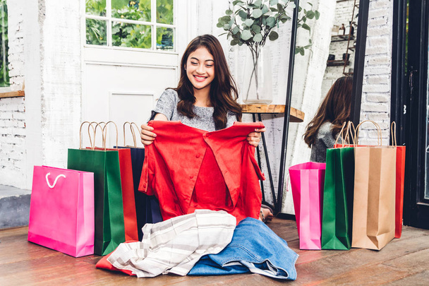 Hermosa mujer de compras y elegir la ropa con colorido bolso de compras sentado en el suelo
  - Foto, imagen