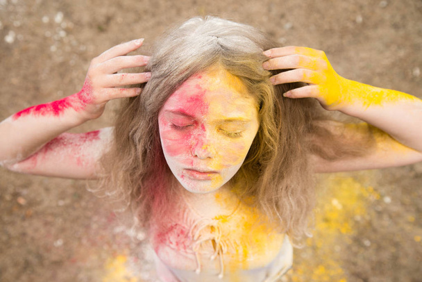 яркая девушка с пышными волосами улыбается, ее волосы, лицо и руки в цветах Холи
  - Фото, изображение