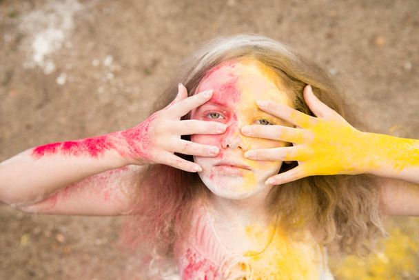 яркая девушка с пышными волосами улыбается, ее волосы, лицо и руки в цветах Холи
  - Фото, изображение