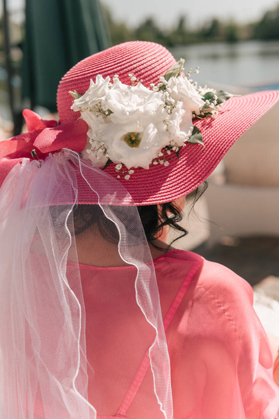 vista trasera de la mujer joven en vestido rosa y sombrero decorado con flores
 - Foto, Imagen