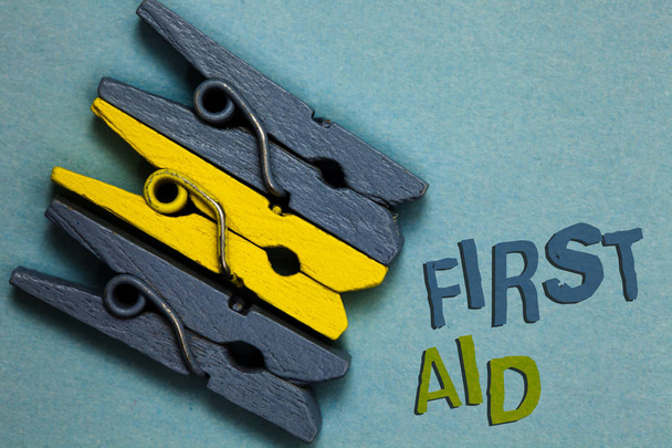 Conceptual hand writing showing First Aid. Business photo text Practise of healing small cuts that no need for medical training Gray yellow vintage clothespins clear background Holding things - Photo, Image