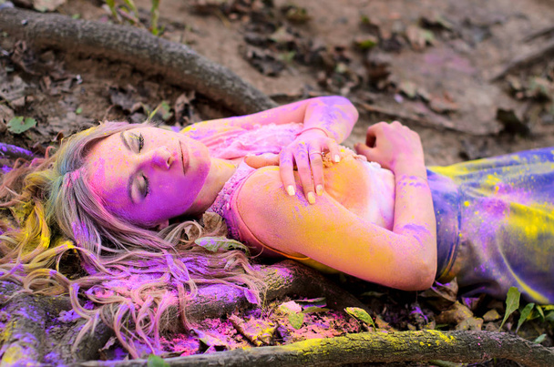 Portret van een meisje, een ingerichte kleuren van Holi, liggend op de grond onder de wortels van bomen - Foto, afbeelding