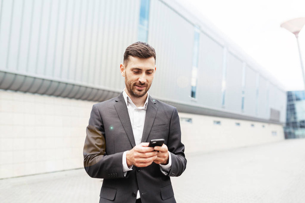 A handsome businessman using a smartphone. working by using smart phone in remote working concept. Business and information technology concept. standing street with city in the background - Foto, Bild
