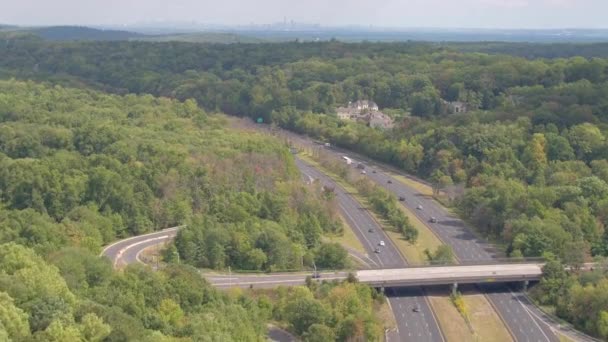 AERIAL ESTABLISHING SHOT: Monikaistainen valtatie, joka johtaa kohti New Yorkin horisonttia. Puoliperävaunuja ja autoja ajamassa pitkin vilkasta moottoritietä vihreiden lähiöiden ohi New Yorkiin
 - Materiaali, video