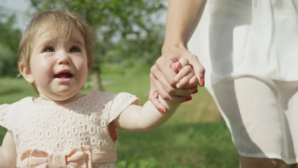 SLOW MOTION, CLOSE UP, DOF : Jolie fille heureuse bébé tenant la main avec la jeune mère et faisant les premiers pas dans le parc local par une journée d'été ensoleillée parfaite. Mère incroyable enseignant fille gaie comment marcher
 - Séquence, vidéo