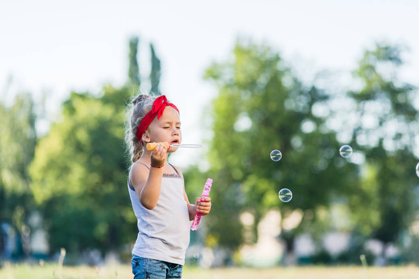Маленькая девочка гуляет по парку и пускает мыльные пузыри летом
 - Фото, изображение