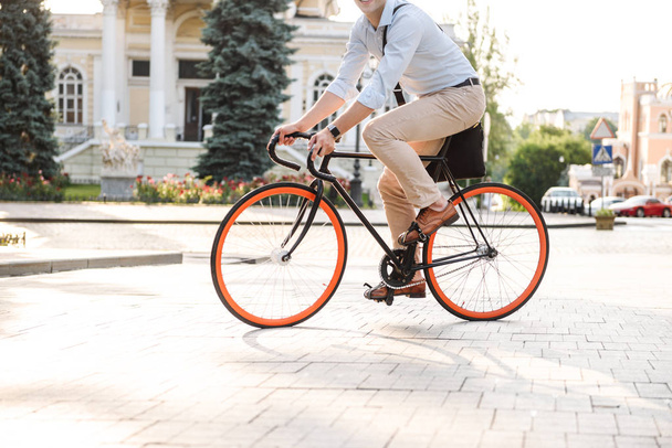 Обрезанный образ молодого стильного мужчины, одетого в рубашку, едущего на велосипеде по городской улице
 - Фото, изображение