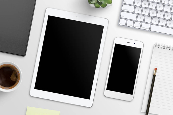 Tablet und Smartphone mit leerem Bildschirm für die Attrappe auf dem Bürotisch, umgeben von Büromaterial. Ansicht von oben. - Foto, Bild