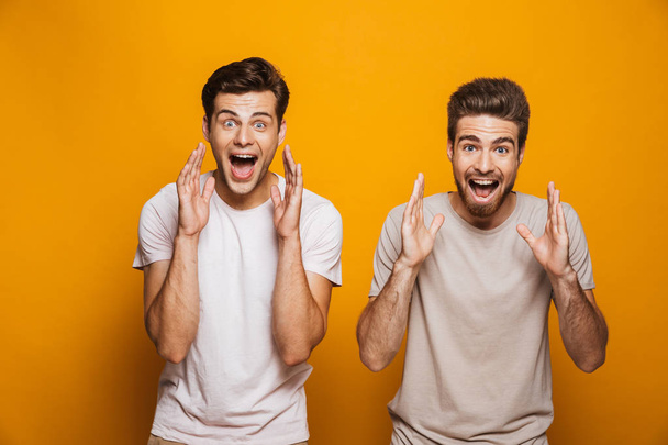 Portrait of a two happy young men best friends screaming loud isolated over yellow background - Foto, afbeelding