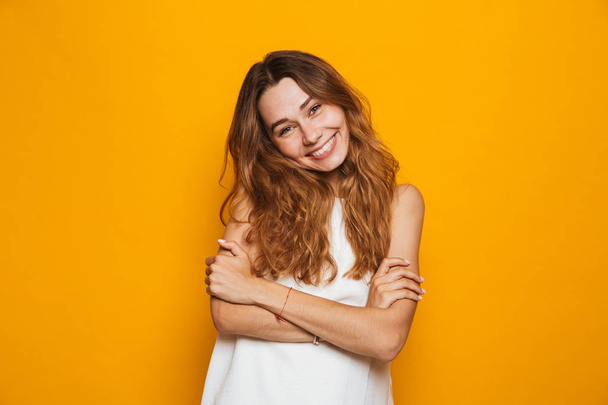 Portrait of a smiling young girl looking at camera isolated over yellow background - Photo, Image