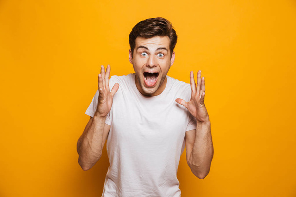 Portrait of an excited young man celebrating success isolated over yellow background - 写真・画像