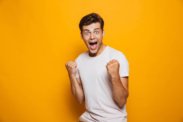 Portrait of an astonished young man celebrating success isolated over yellow background - Fotoğraf, Görsel