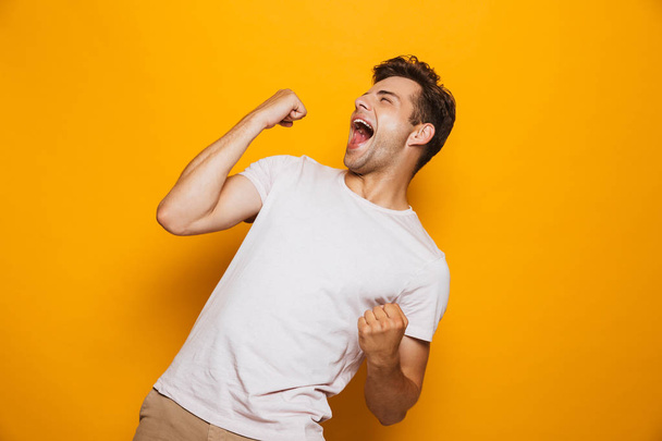 Portrait of a joyful young man celebrating success isolated over yellow background - Foto, afbeelding