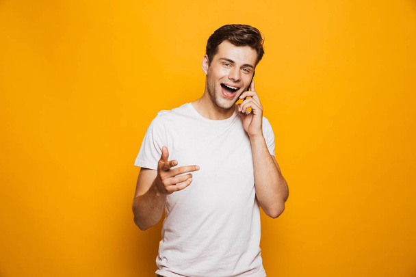 Portrait of a happy young man talking on mobile phone isolated over yellow background - Foto, Imagem