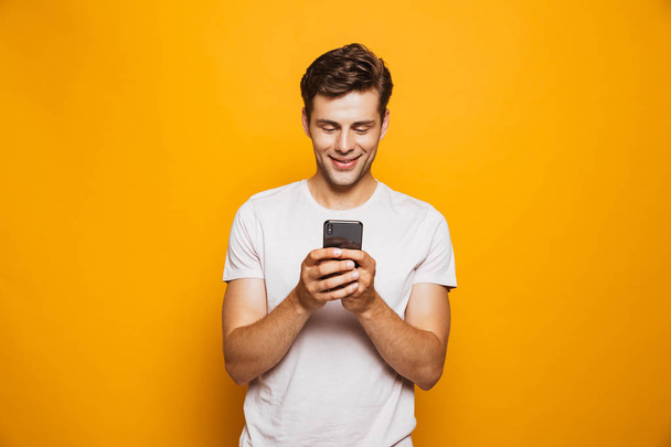 Portrait of a happy young man using mobile phone isolated over yellow background - Foto, imagen