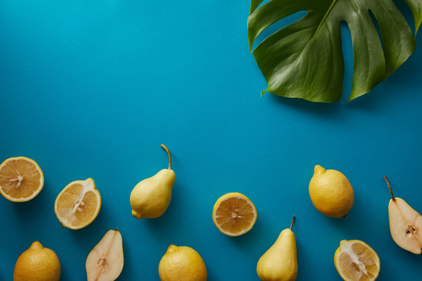 top view of palm tree leaf, pears and lemons on blue surface - Foto, afbeelding