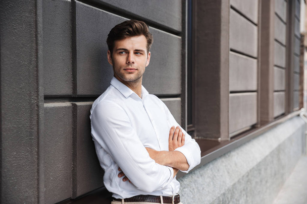 Portrait of a confident young formal dressed man leaning on a wall outdoors with arms folded - Photo, image