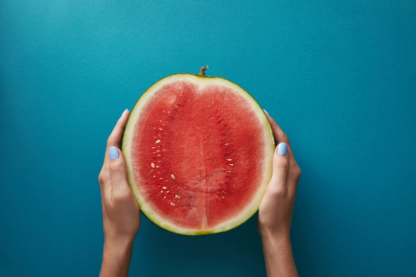 cropped image of woman holding half of watermelon above blue surface  - Foto, Imagem