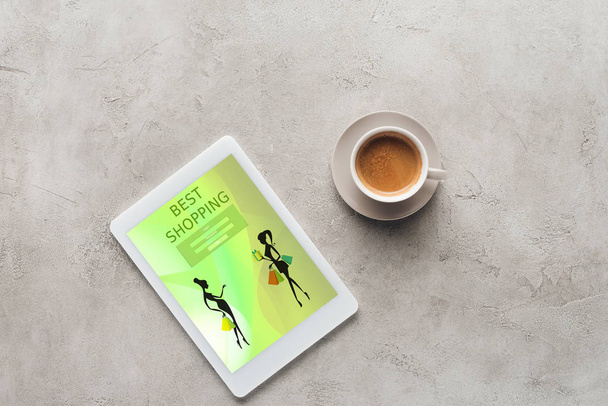 Draufsicht auf Tasse Kaffee und Tablet mit bester Shopping-App auf dem Bildschirm auf Betonoberfläche - Foto, Bild
