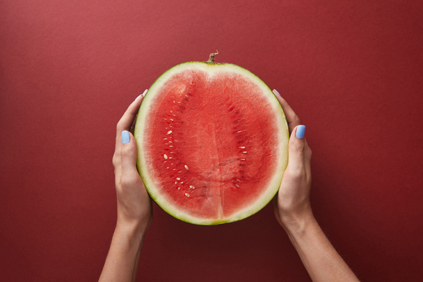 cropped image of woman holding half of watermelon above red surface  - Foto, Imagem