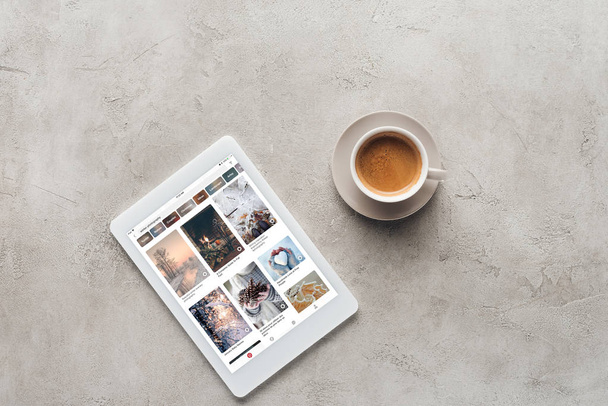 top view of cup of coffee and tablet with pinterest website on screen on concrete surface - Foto, afbeelding
