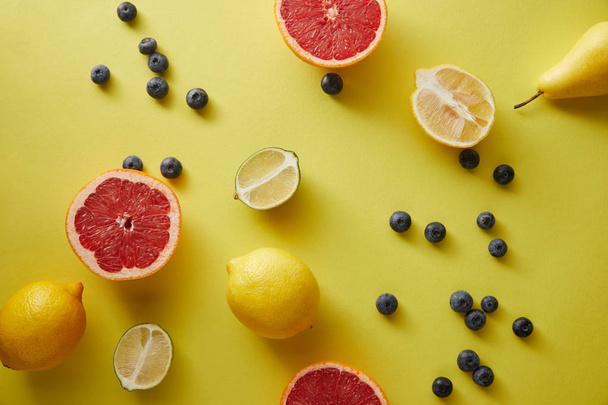 top view of grapefruits, lemons, limes and blueberries on yellow surface - Photo, image
