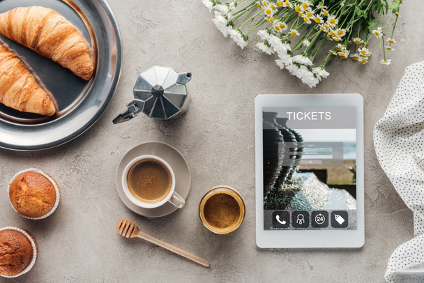 bovenaanzicht van koffie met gebak en tablet met tickets app op scherm op betonnen ondergrond - Foto, afbeelding