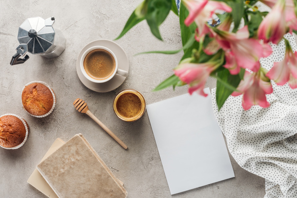 top view of delicious coffee with muffins, blank paper and alstroemeria bouquet on concrete surface - Photo, Image
