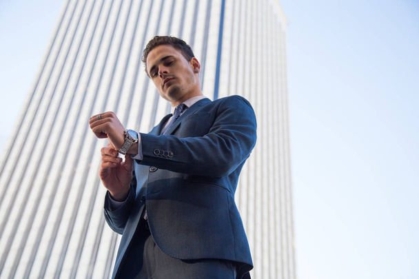 Desde abajo vista de hombre con estilo en traje elegante posando con confianza en el fondo de rascacielos de oficina moderna
  - Foto, Imagen
