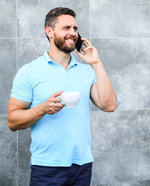 Man drink cappuccino speak phone grey wall background. Even if you drink coffee on the go each sip is little break in your day and little moment of self care. Reasons entrepreneurs drink coffee - Fotoğraf, Görsel