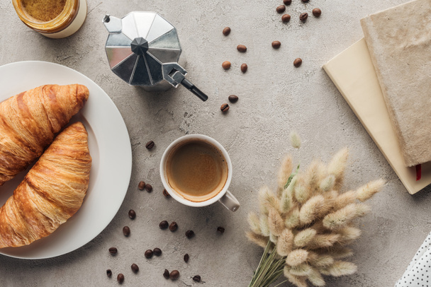vista superior de la taza de café con croissants y moka pot en la superficie de hormigón con ramo de lagurus ovatus y libro
 - Foto, imagen