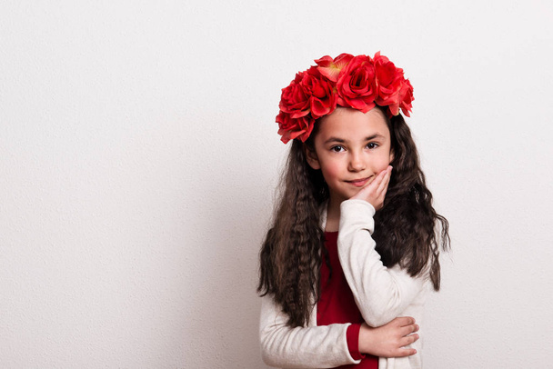 Une petite fille avec un bandeau de fleurs debout dans un studio, le menton posé sur sa main
. - Photo, image