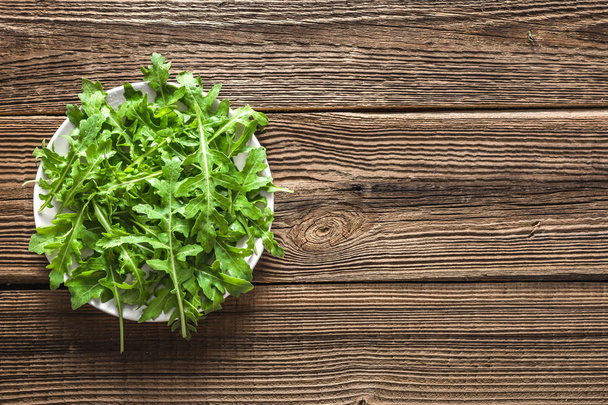 Green vegetable, leaves of arugula on plate on wooden table, healthy food concept - Foto, imagen