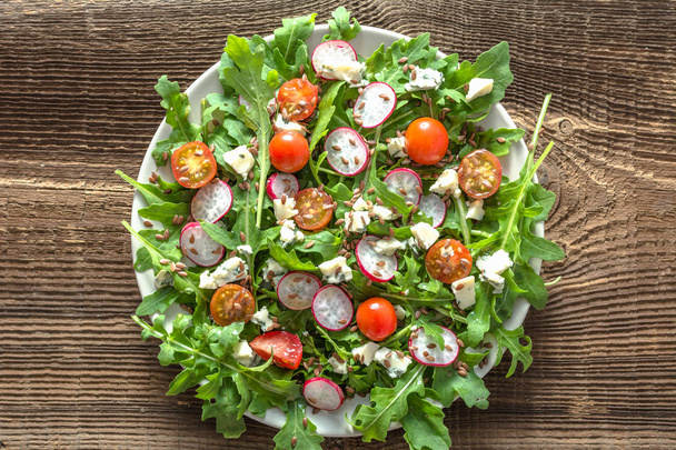 Healthy diet. Vegetable Fresh salad with arugula leaves, tomato, radish and seeds. Dietary appetizer or lunch on plate, vegetarian food concept. - Photo, Image