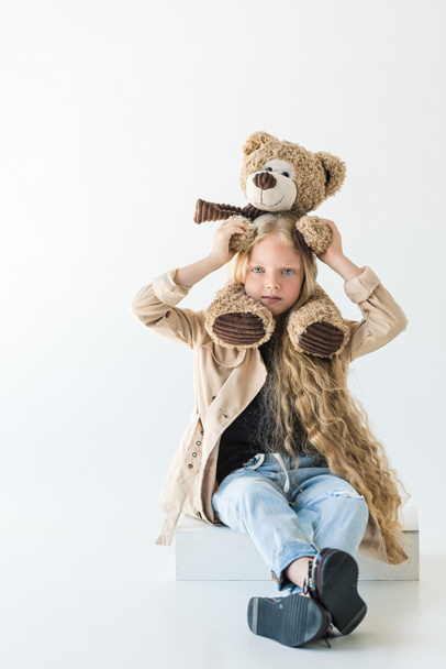 beautiful stylish kid holding teddy bear and looking at camera isolated on white  - Фото, зображення