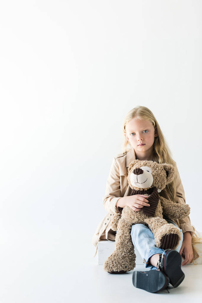 full length view of beautiful stylish kid holding teddy bear and looking at camera isolated on white - Photo, Image