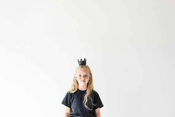 adorable child with long curly hear wearing black crown and smiling at camera isolated on white - Foto, Imagen