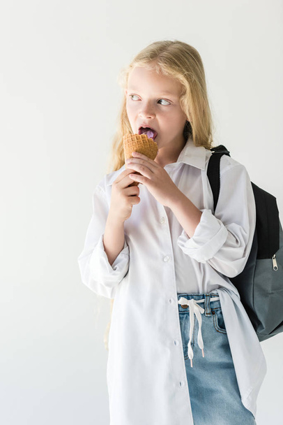 beautiful kid with backpack eating ice cream and looking away isolated on white - Fotoğraf, Görsel