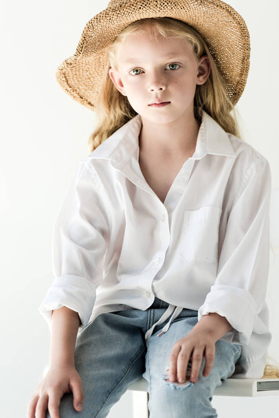 portrét krásné malé dítě v proutěné klobouk sedí a při pohledu na fotoaparát na bílém   - Fotografie, Obrázek