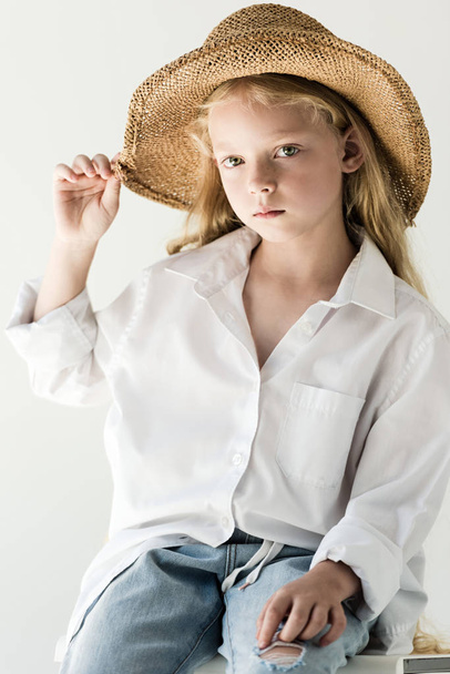 hermoso niño pequeño en sombrero de paja sentado y mirando a la cámara en blanco
   - Foto, imagen